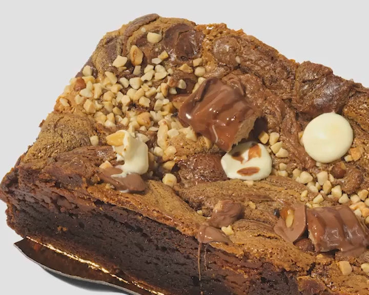 Load video: Close-up video panning from left to right across a Filthy Footlong Kinder brownie, showing chocolate topping and detailed texture.